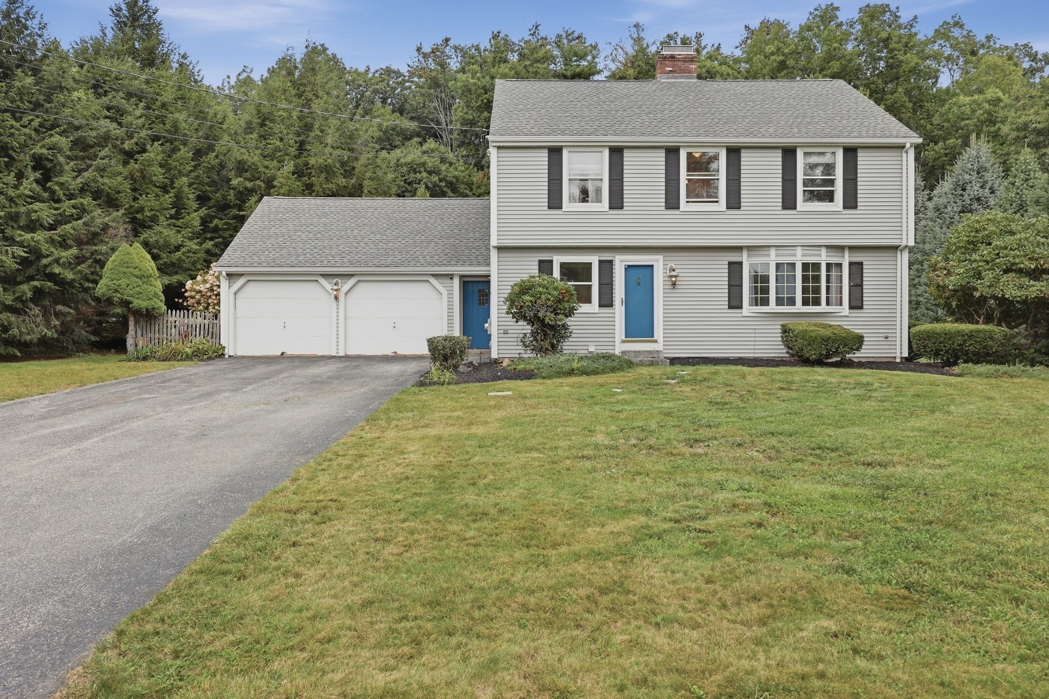 Two-story gray house with a blue front door, attached garage, and broad lawn.