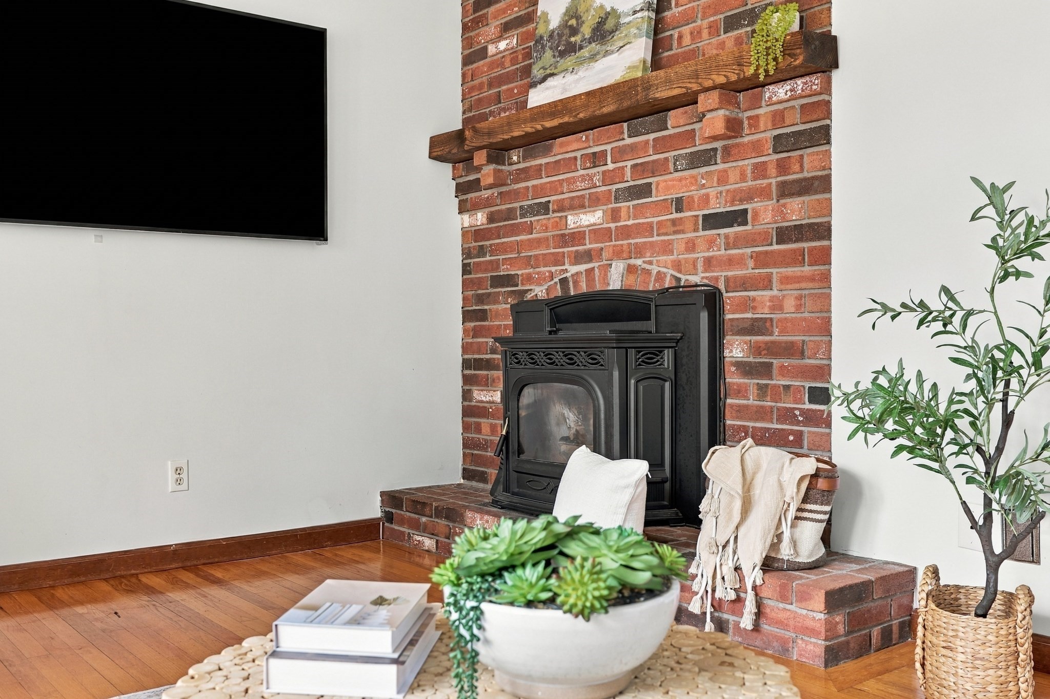 Living room with a black stove in a red brick fireplace and a thick wooden mantel.