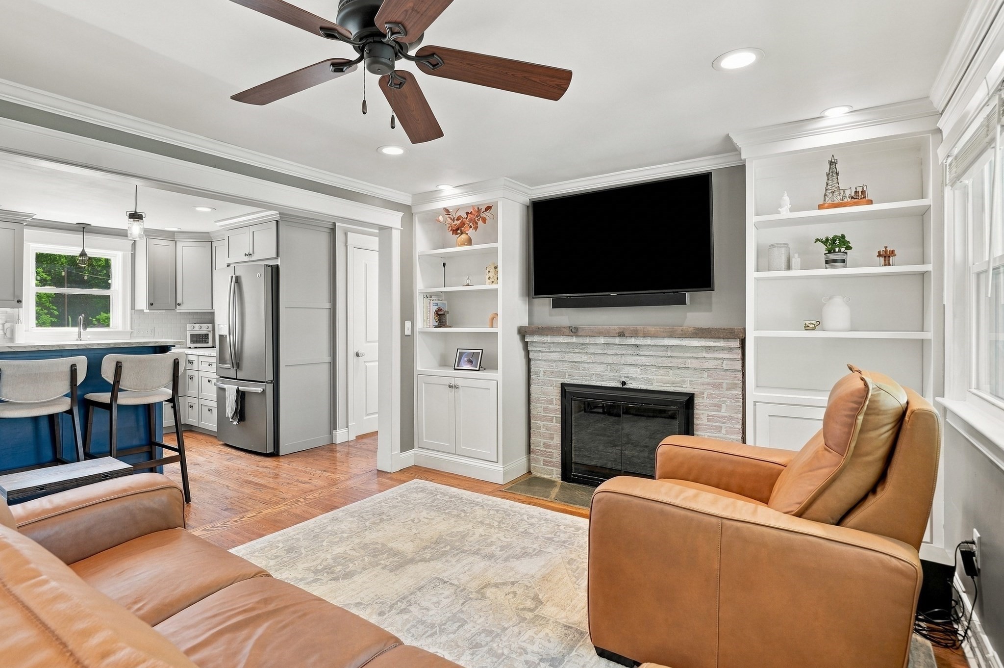 Open-plan living room and kitchen with a white brick fireplace, built-in shelves, and brown leather seating.
