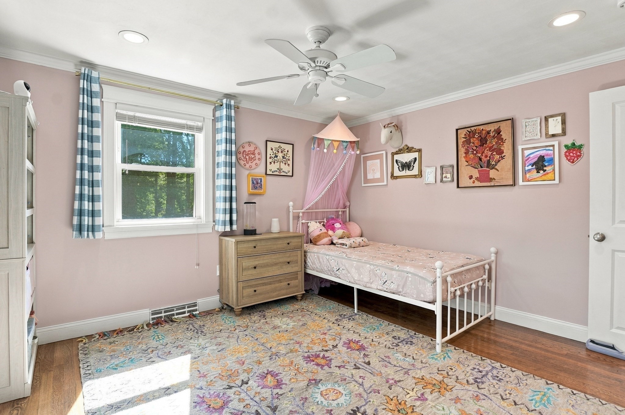 Child's bedroom with a pink canopy bed, colorful wall art, and a large patterned rug.