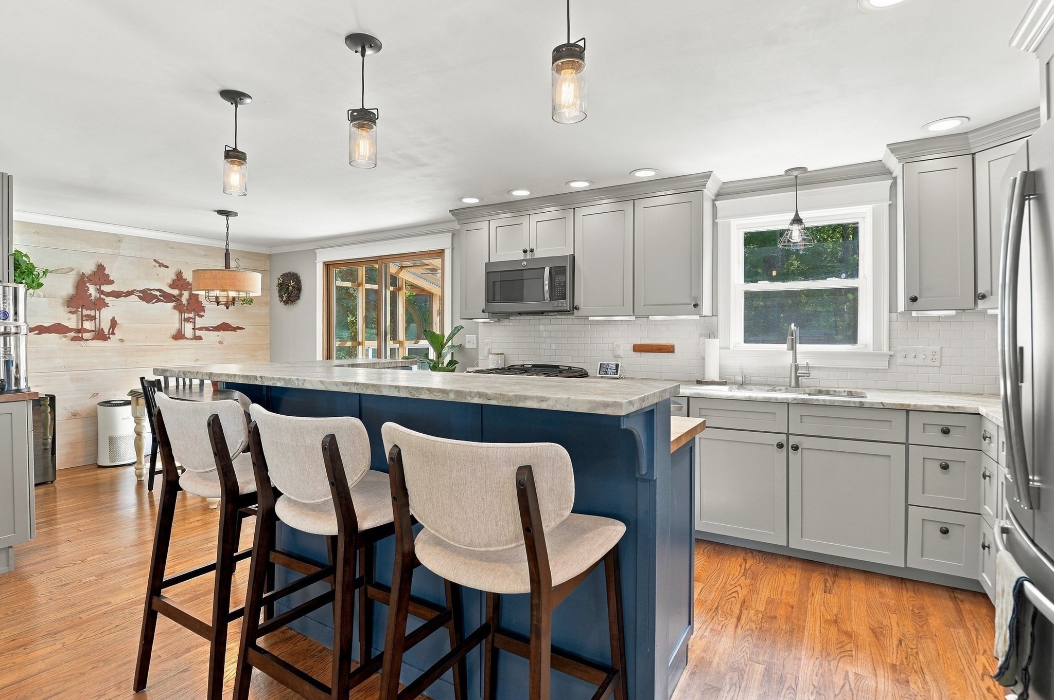 Kitchen with a large navy island, stone countertop, gray cabinets, and wood floors.