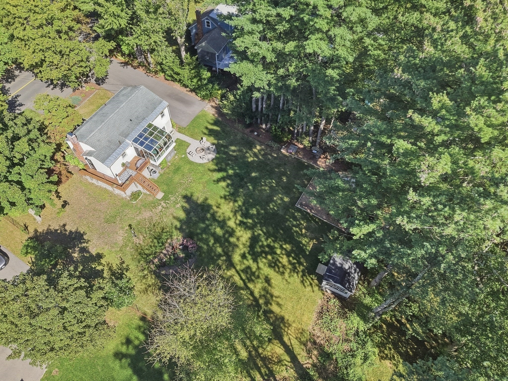 Aerial view of a white house with a glass sunroom, deck, patio, and tree-lined yard.