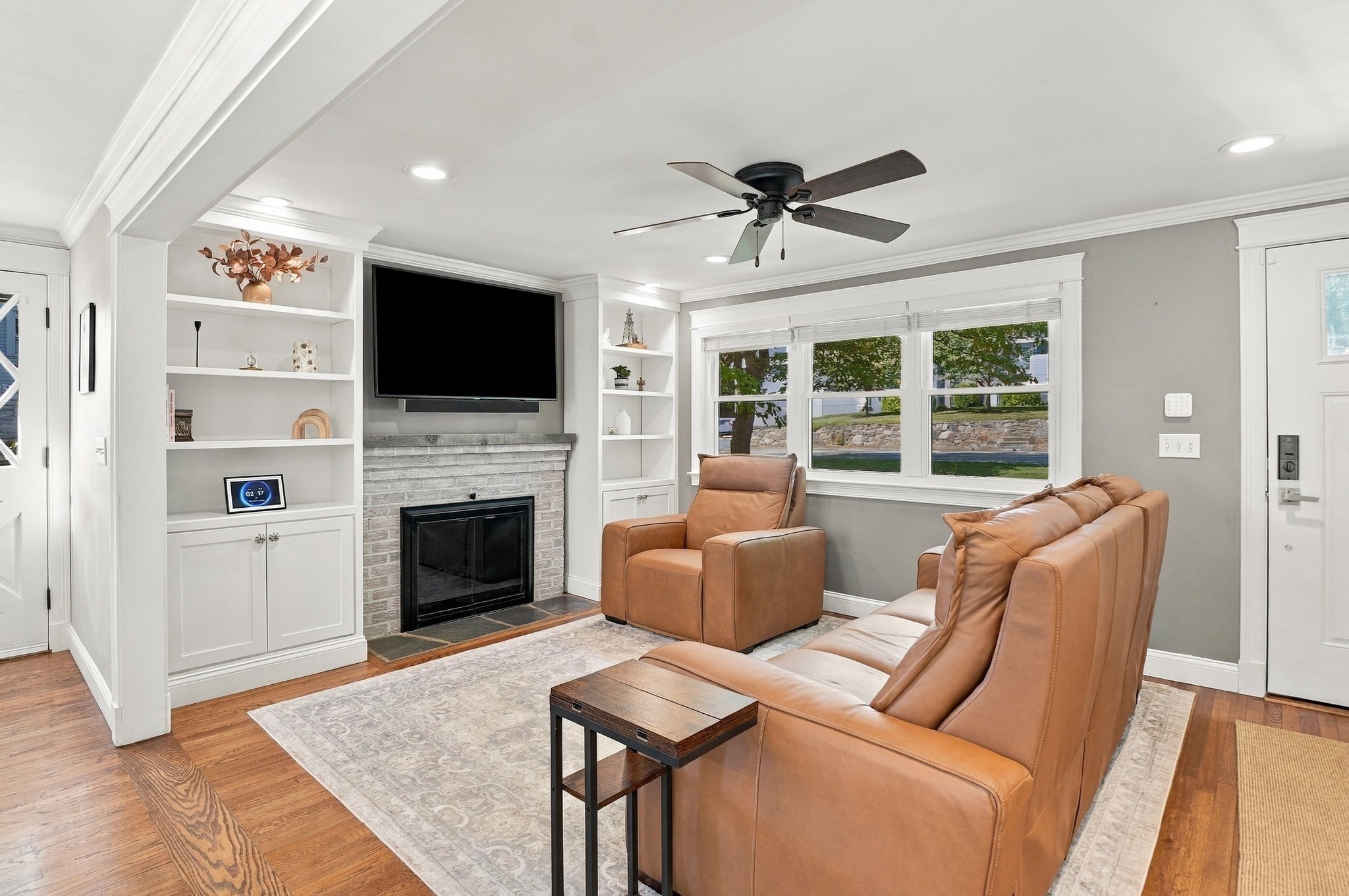 Living room with tan leather seating, built-in shelving, and a white brick fireplace.