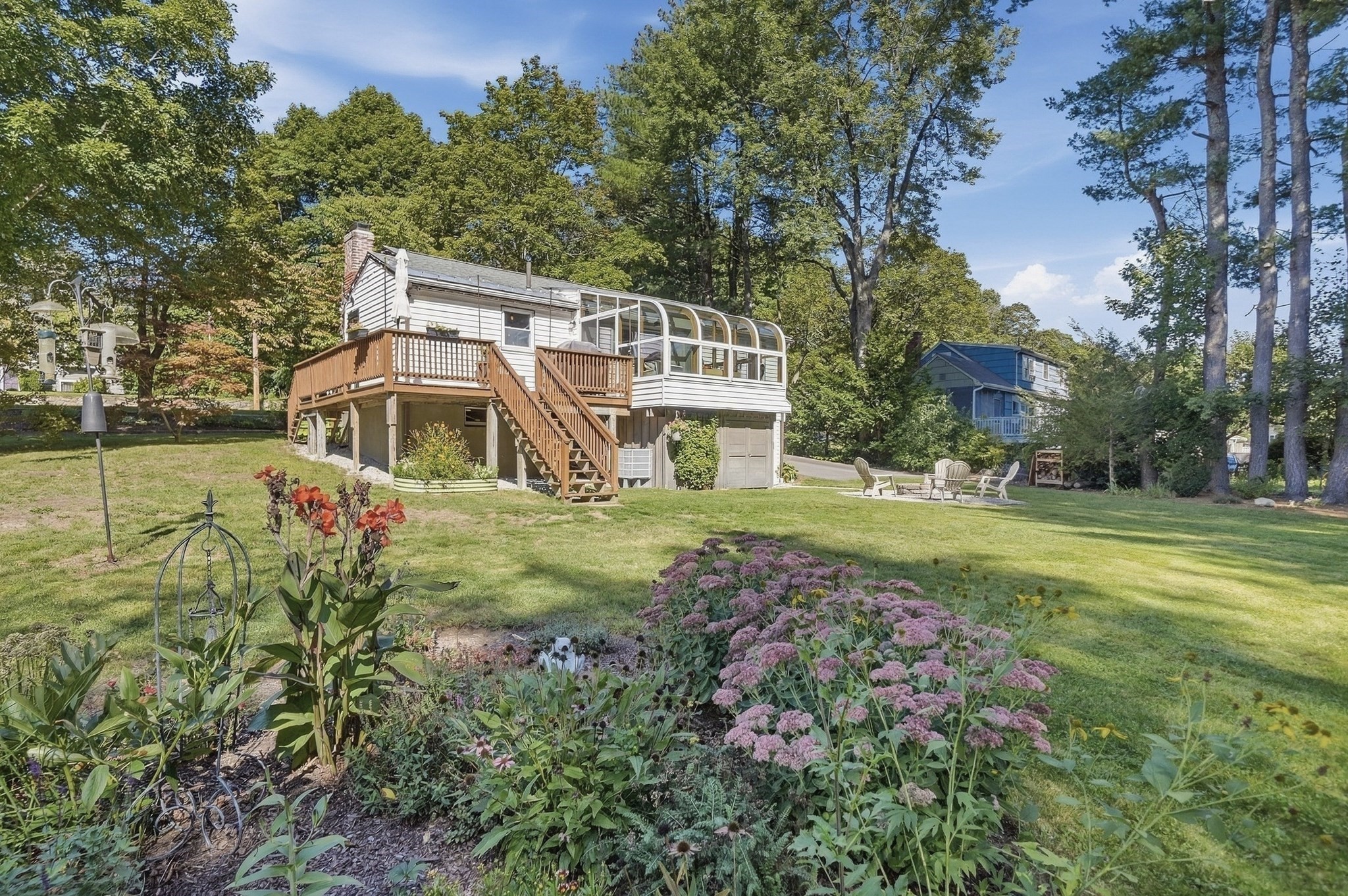 Raised white home with an enclosed sunroom, wooden deck, and flower garden.