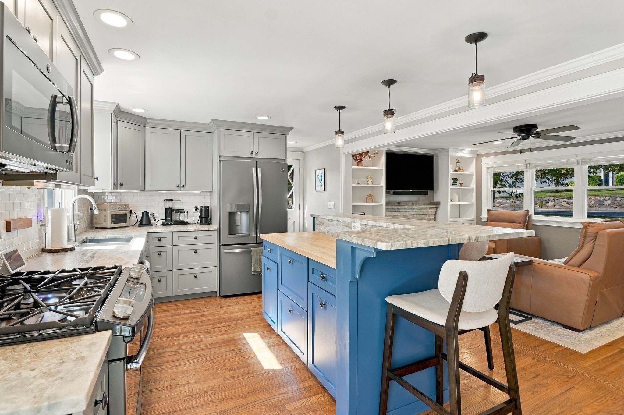 Open-plan kitchen with a blue island and stone countertop beside a furnished living area.