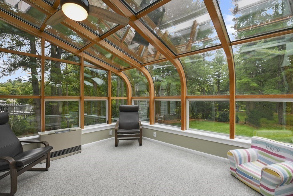 Sunroom with a curved glass ceiling, wood-framed windows, and views of trees and lawn.