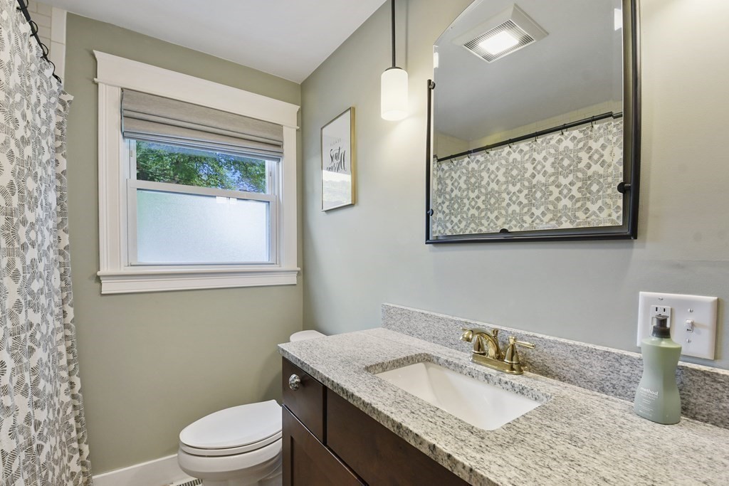 Bathroom vanity with a speckled granite counter, brass faucet, and patterned shower curtain.