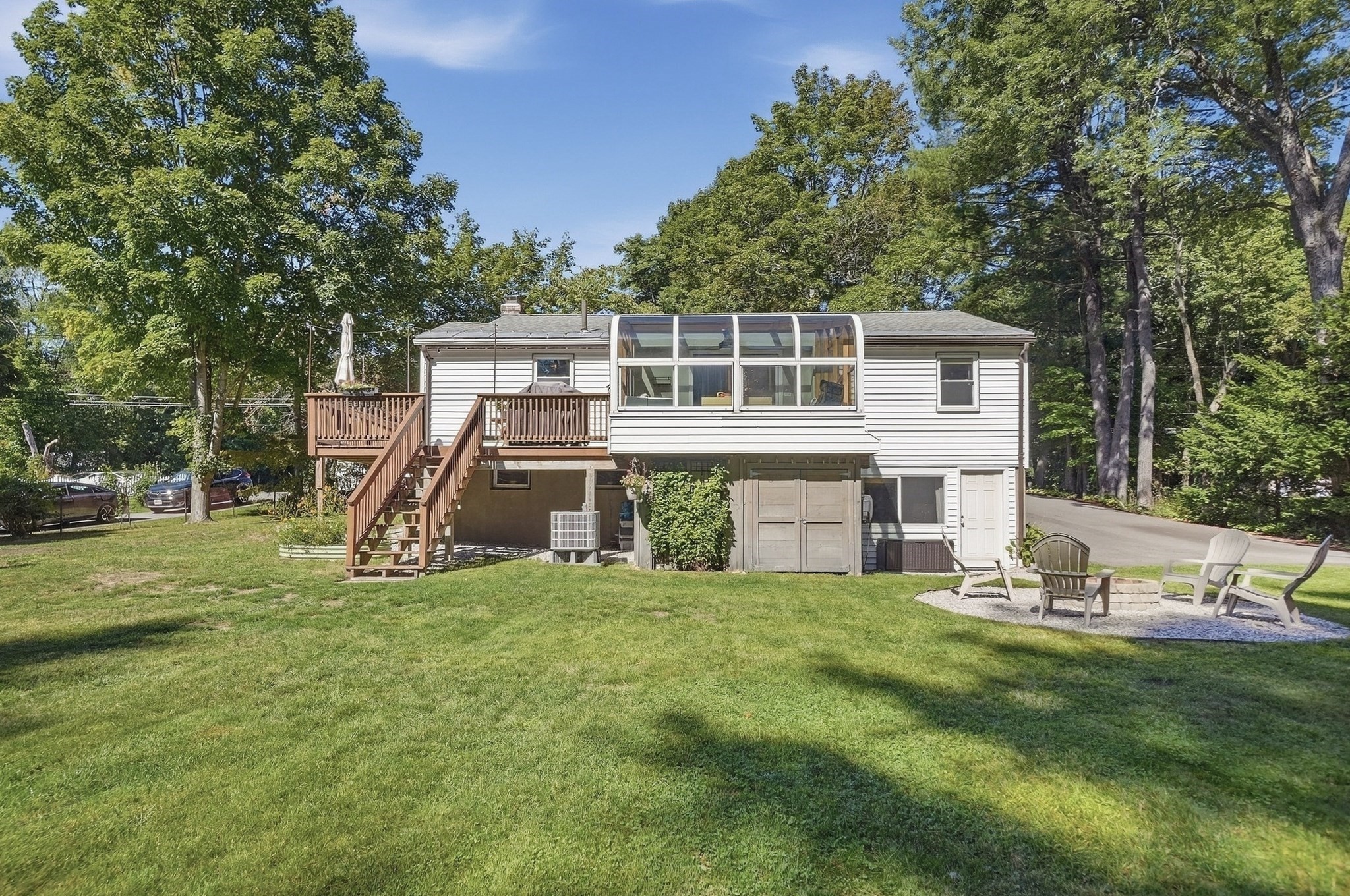 Rear exterior of a house with an enclosed sunroom, raised deck, and lawn fire pit.