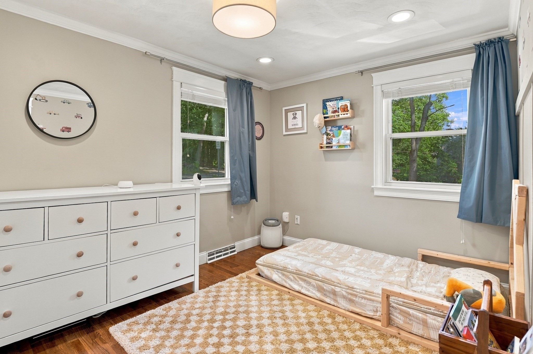 Child’s bedroom with blue curtains, a white dresser, and a low wooden bed.