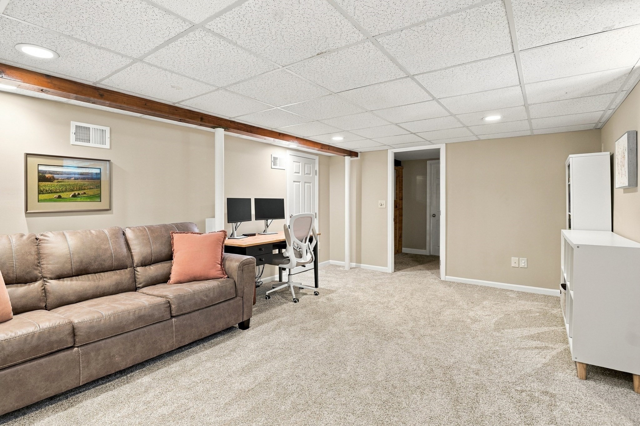 Furnished basement room with a sectional sofa and a desk with dual monitors.
