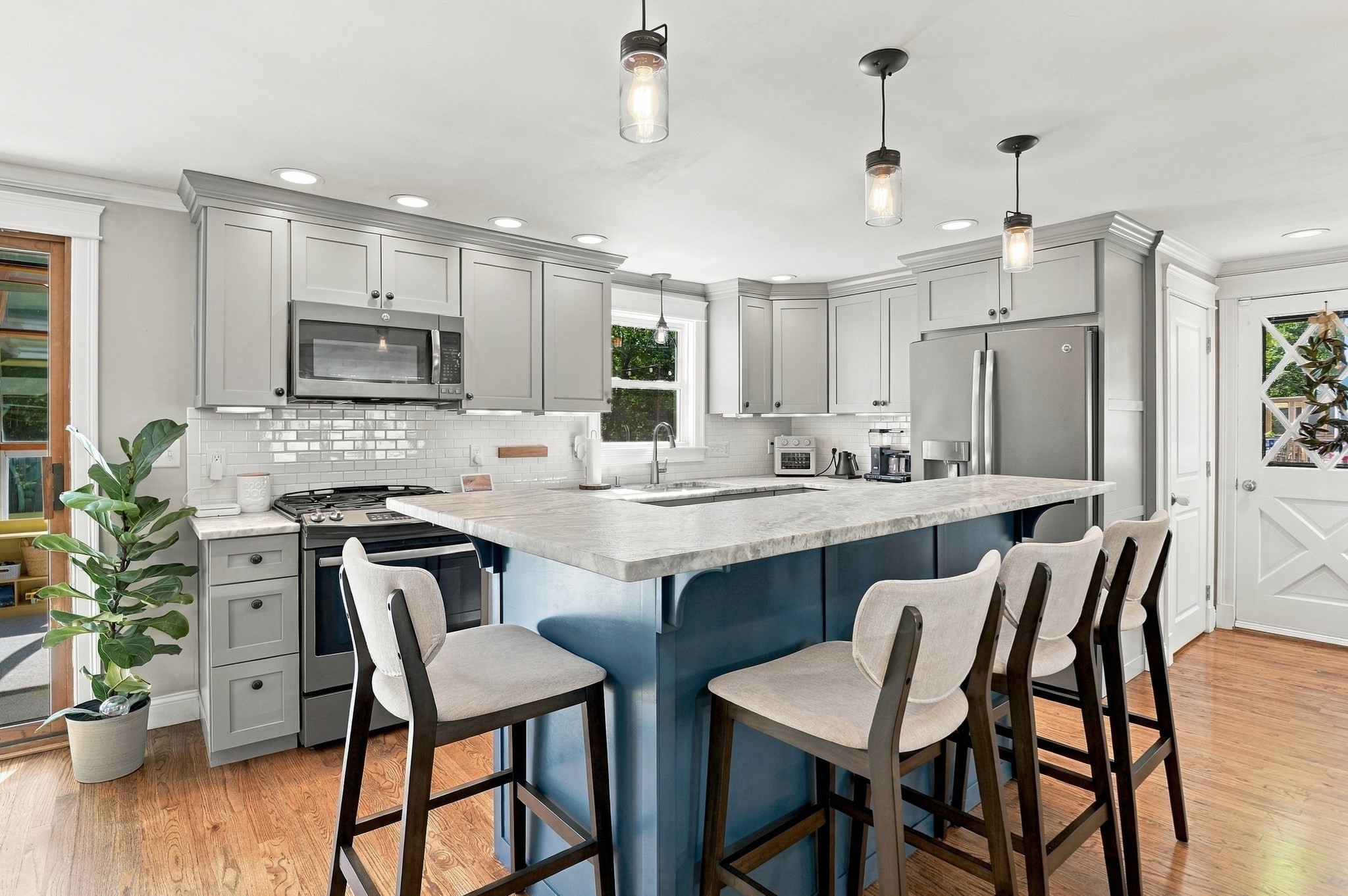 Bright kitchen with gray cabinets, stainless appliances, and a large blue island lined with upholstered stools.