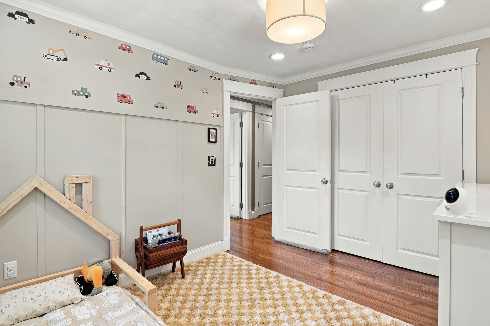 Child's bedroom with colorful vehicle decals, a low wooden bed, and white closet doors.
