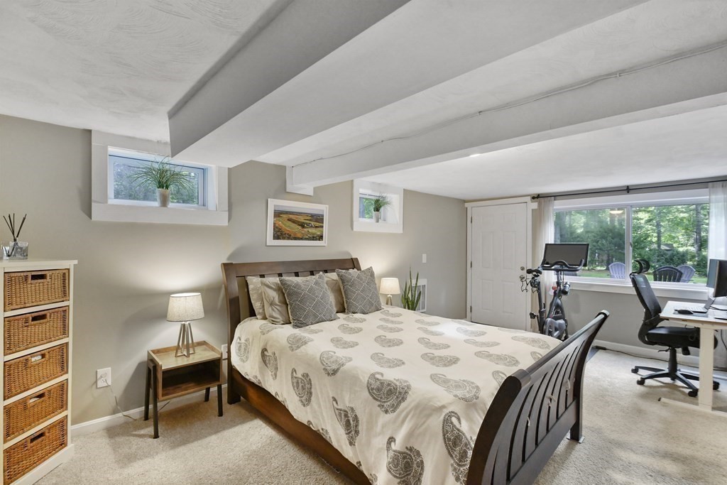 Furnished bedroom with exposed ceiling beams, a desk, exercise bike, and large window overlooking trees.