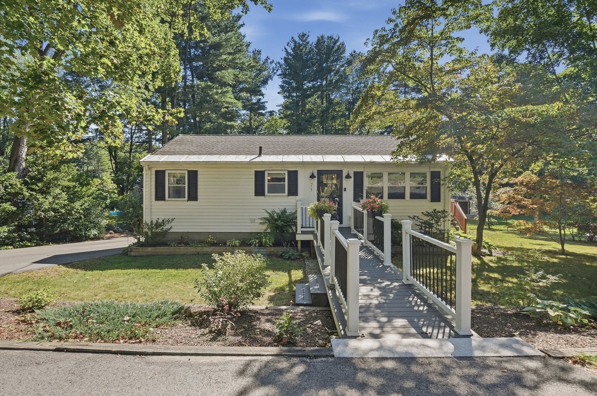 Single-story cream home with dark shutters and a railed ramp leading to the front entrance.