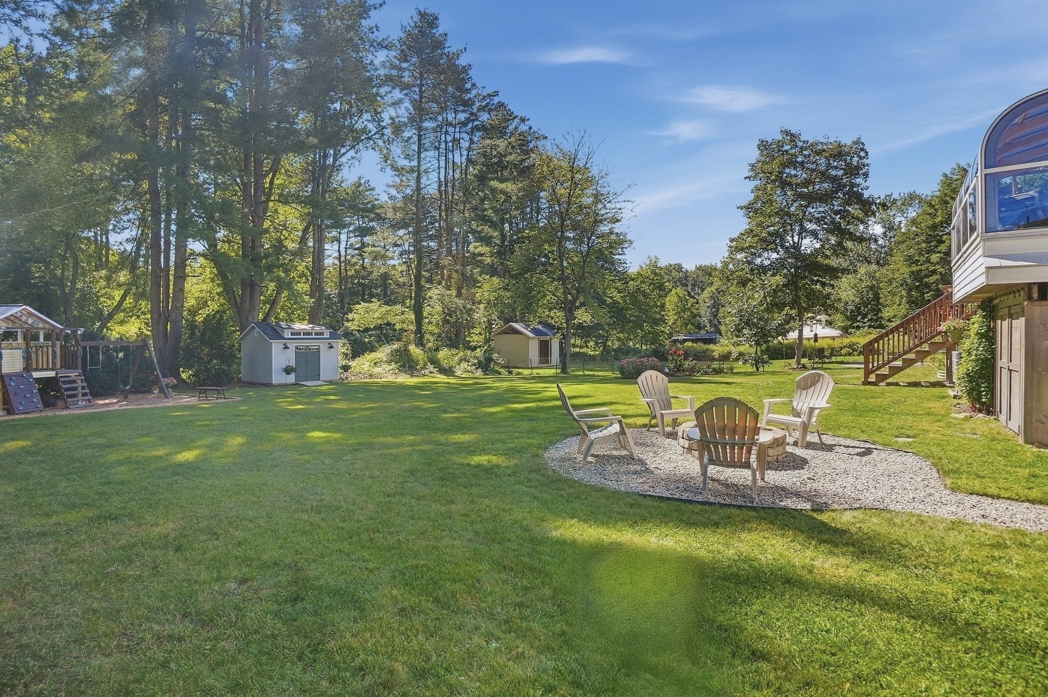 Spacious backyard with a gravel fire pit seating area, playset, storage sheds, and a raised deck.
