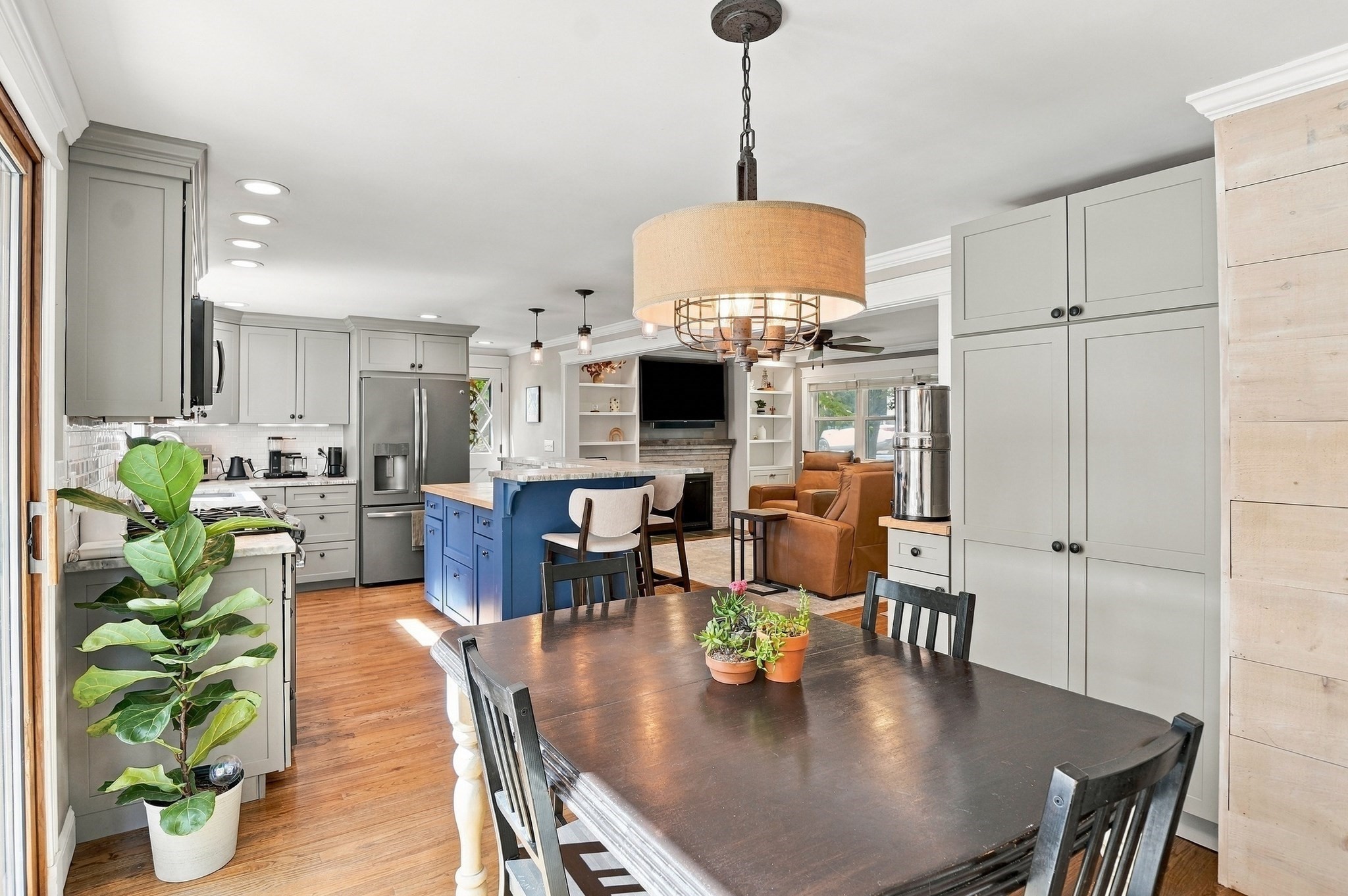 Open kitchen and dining area with gray cabinets, blue island, and adjoining living room with tan leather seating.