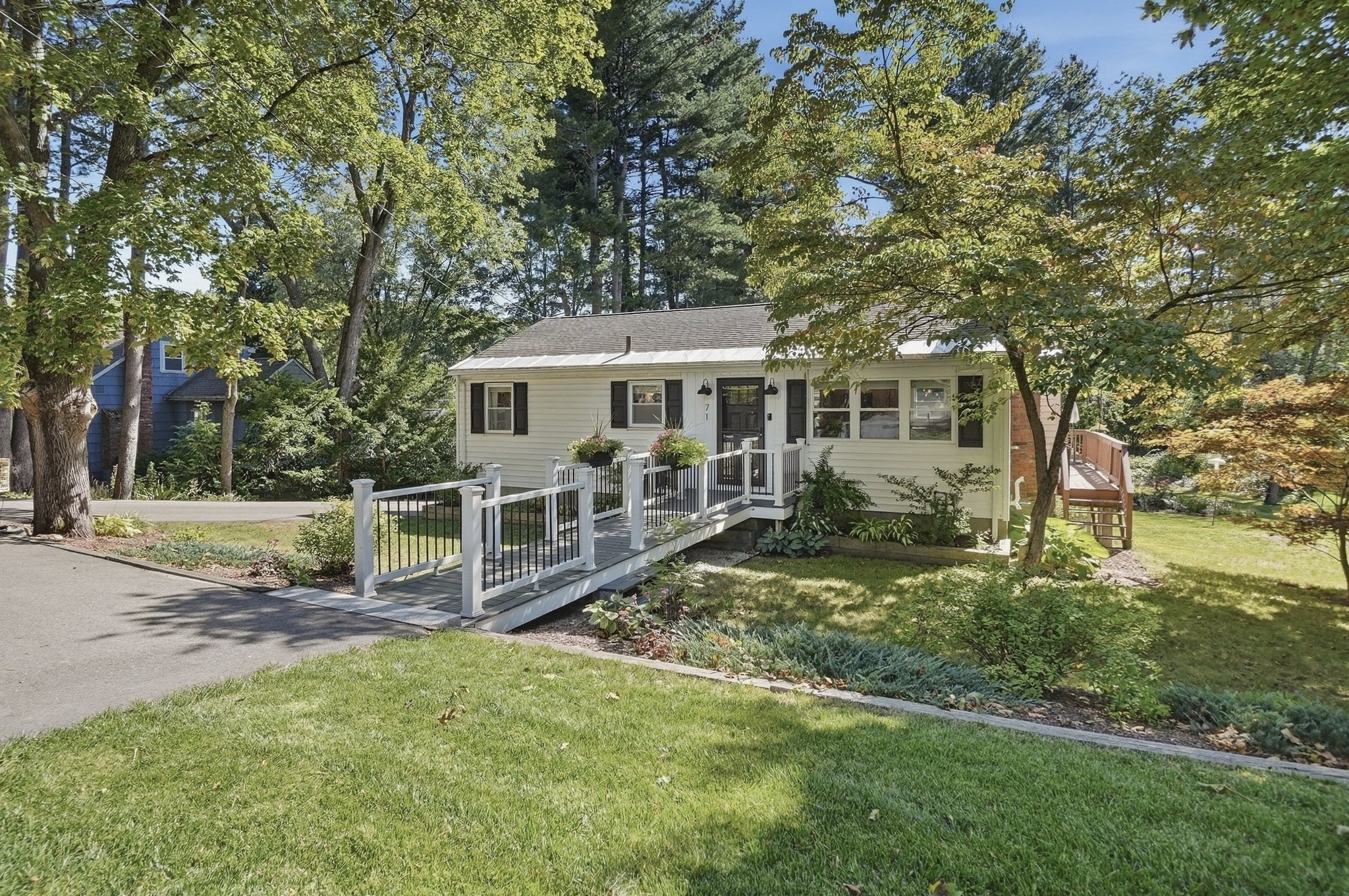 Single-story house with a wide accessibility ramp, mature trees, and landscaped front yard.