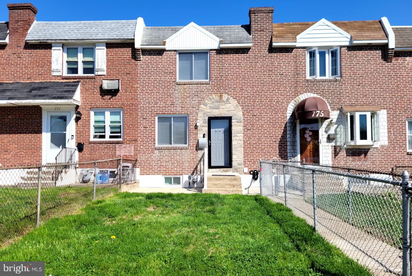 Red-brick townhouse with a stone-arched entry and fenced front lawn.
