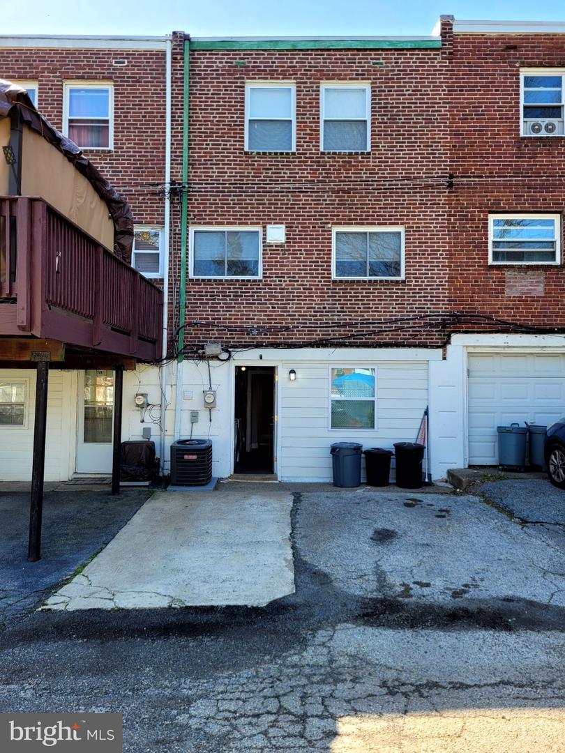 Rear exterior of a brick row building with white siding, a garage, and a paved driveway.