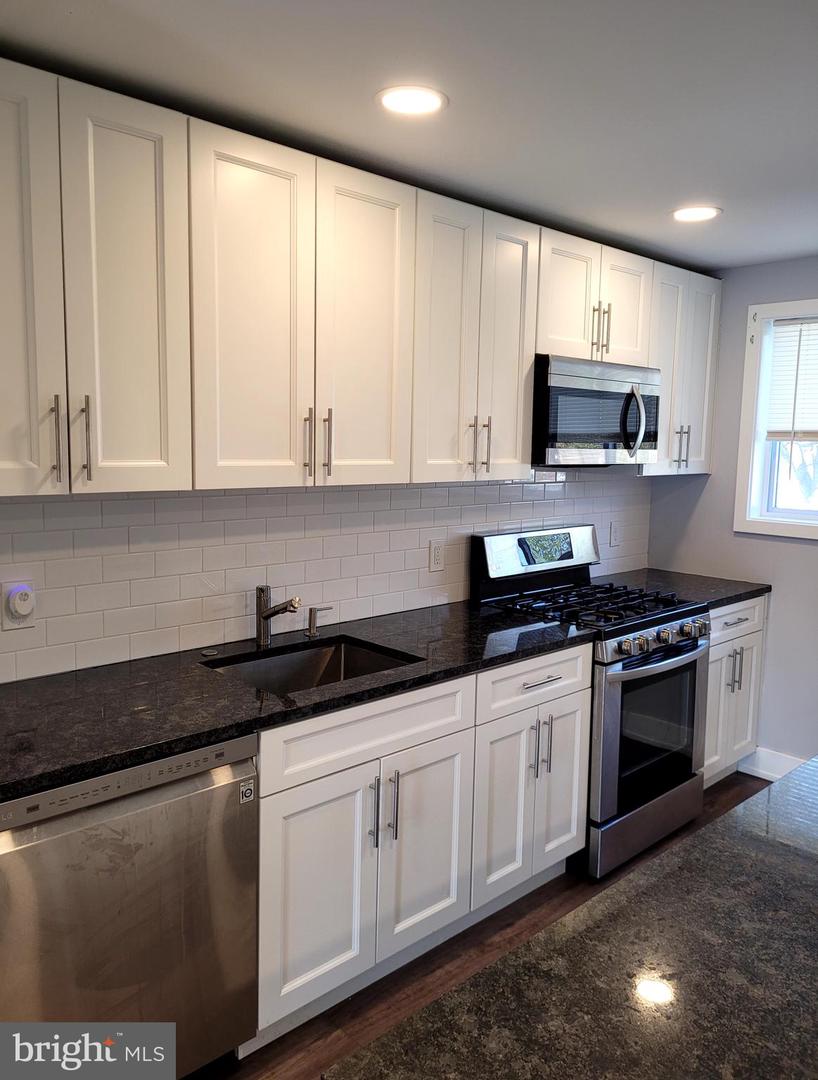 Kitchen with white cabinets, dark countertops, subway tile backsplash, and stainless steel appliances.