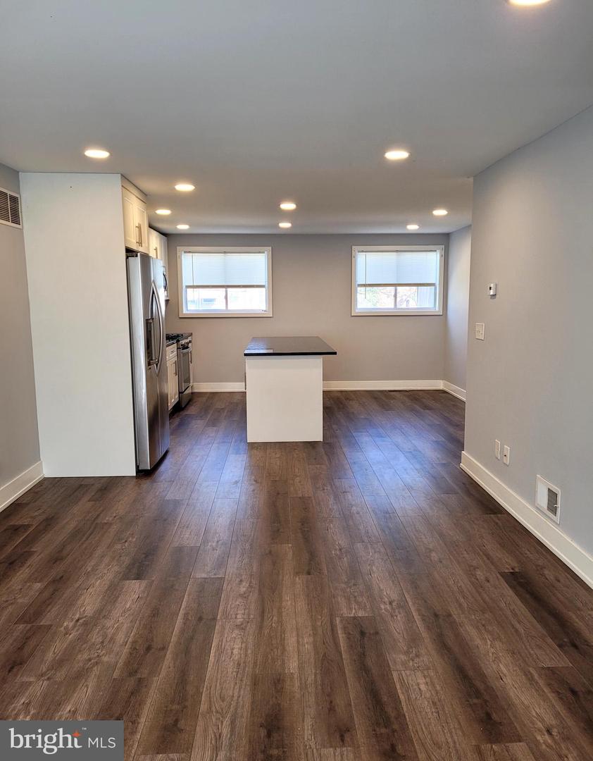 Vacant kitchen with a central island, stainless steel refrigerator, and dark wood-look flooring.