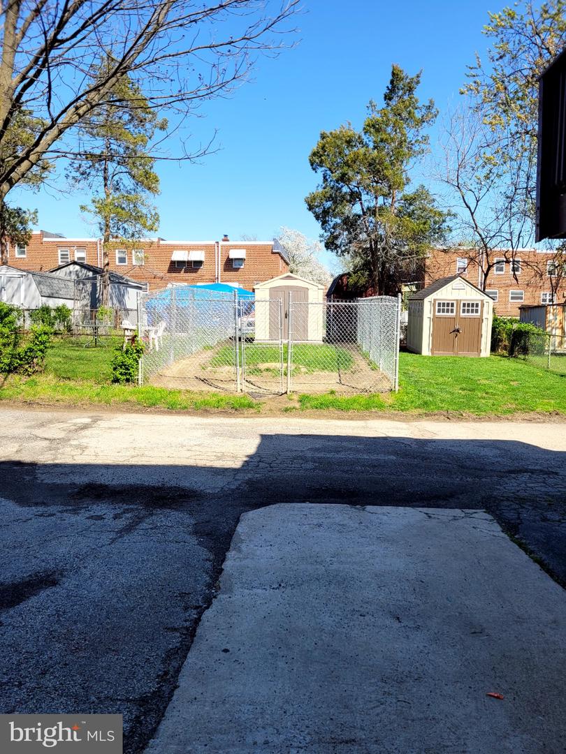 Fenced backyard with two sheds and neighboring brick row houses beyond.