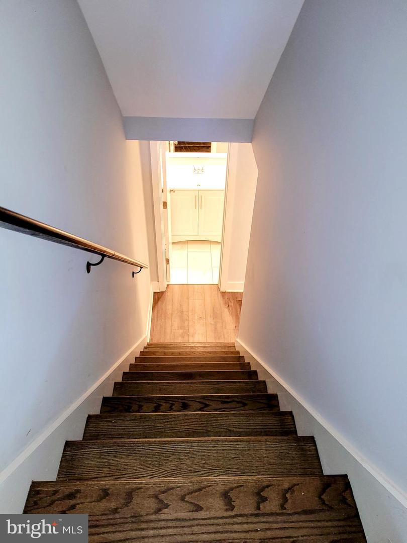 Dark wood staircase descends to a landing with a bright bathroom vanity beyond.