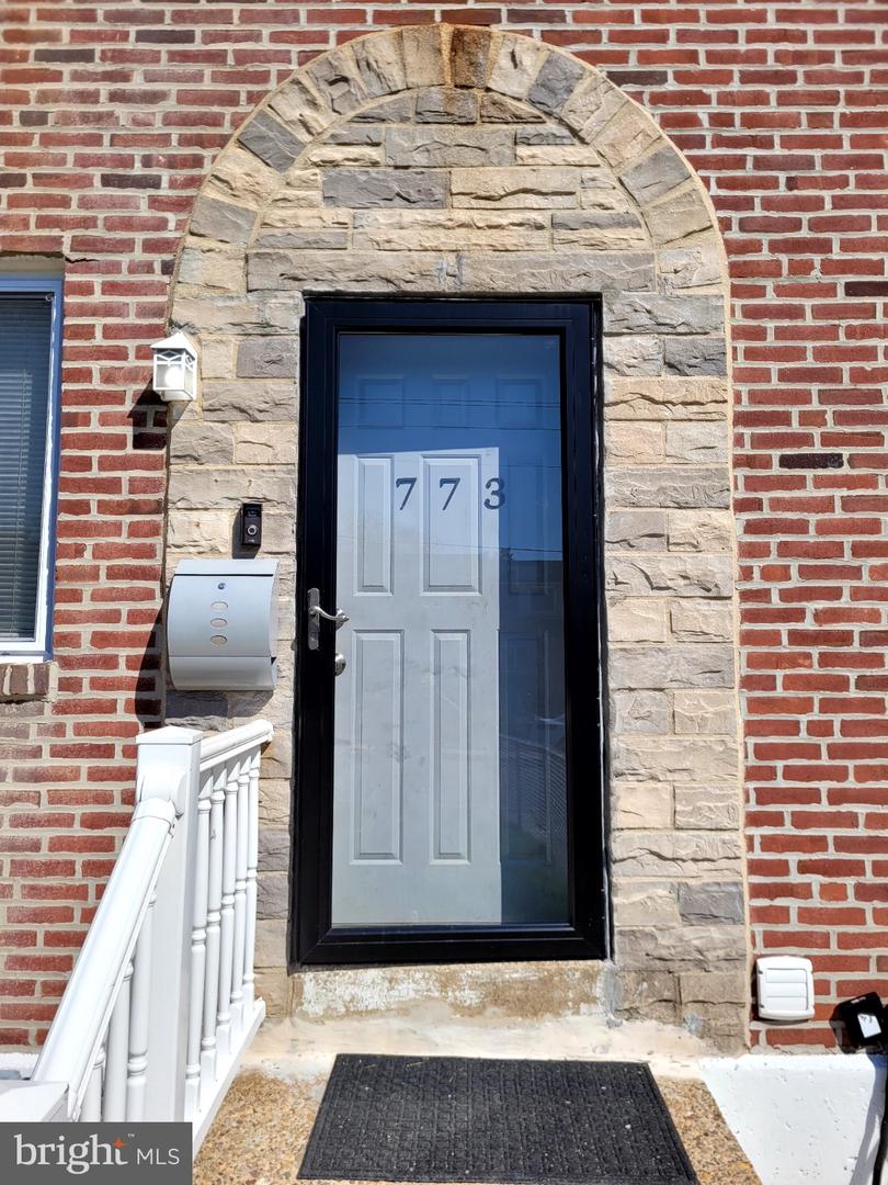 Front entrance with a stone arch, red brick facade, black storm door, and white railing.