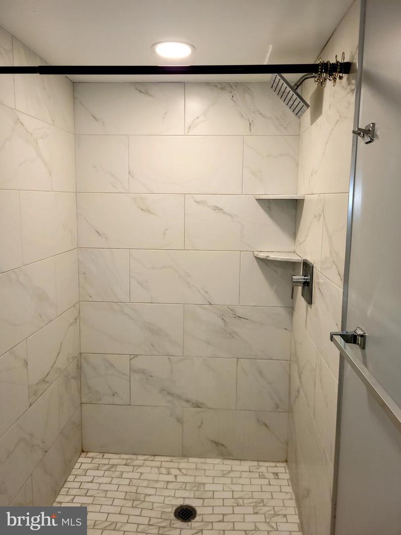 Walk-in shower with marble-look wall tile, corner shelves, and a mosaic tile floor.