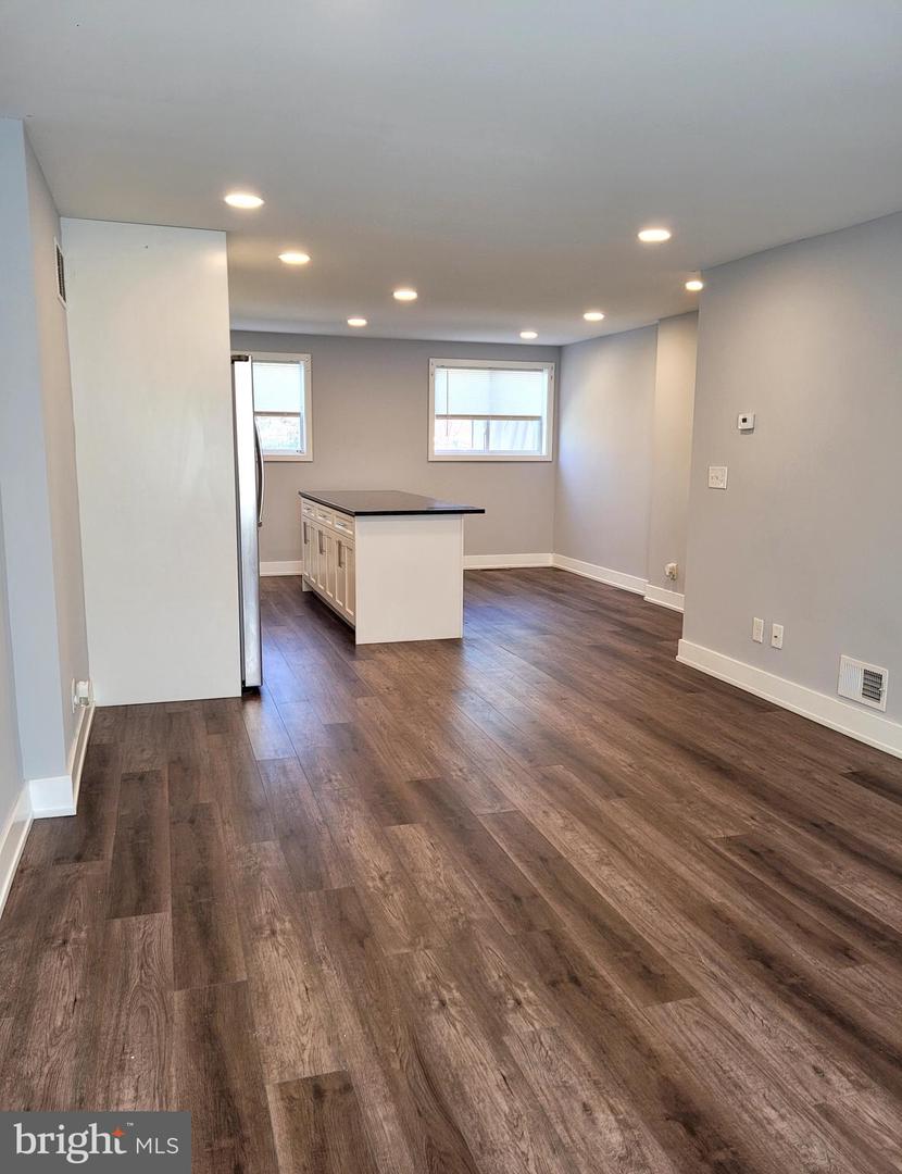 Unfurnished kitchen and living area with a central island, recessed lights, and dark wood-look floors.