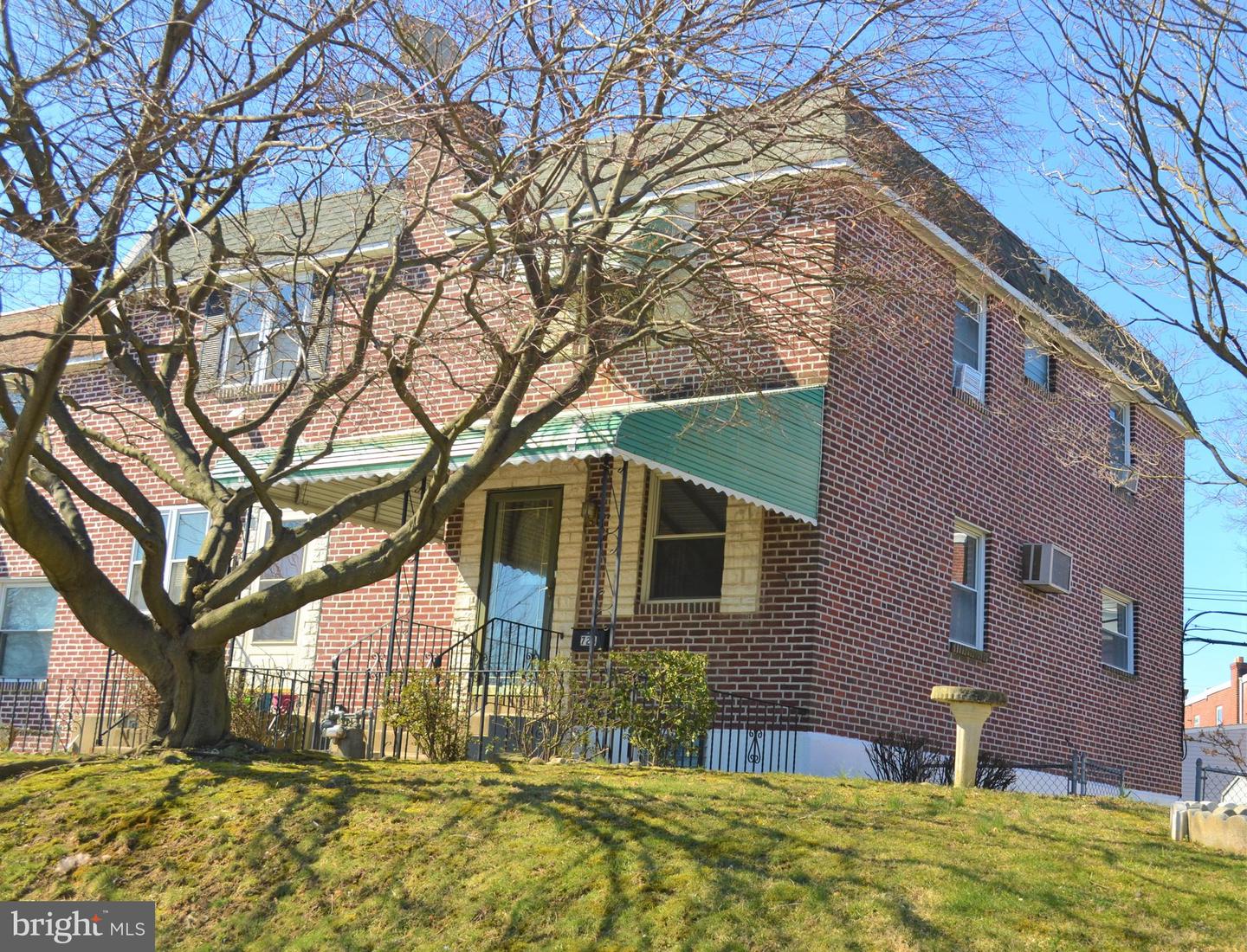 Two-story red-brick house with a covered porch, partly obscured by a large leafless tree.