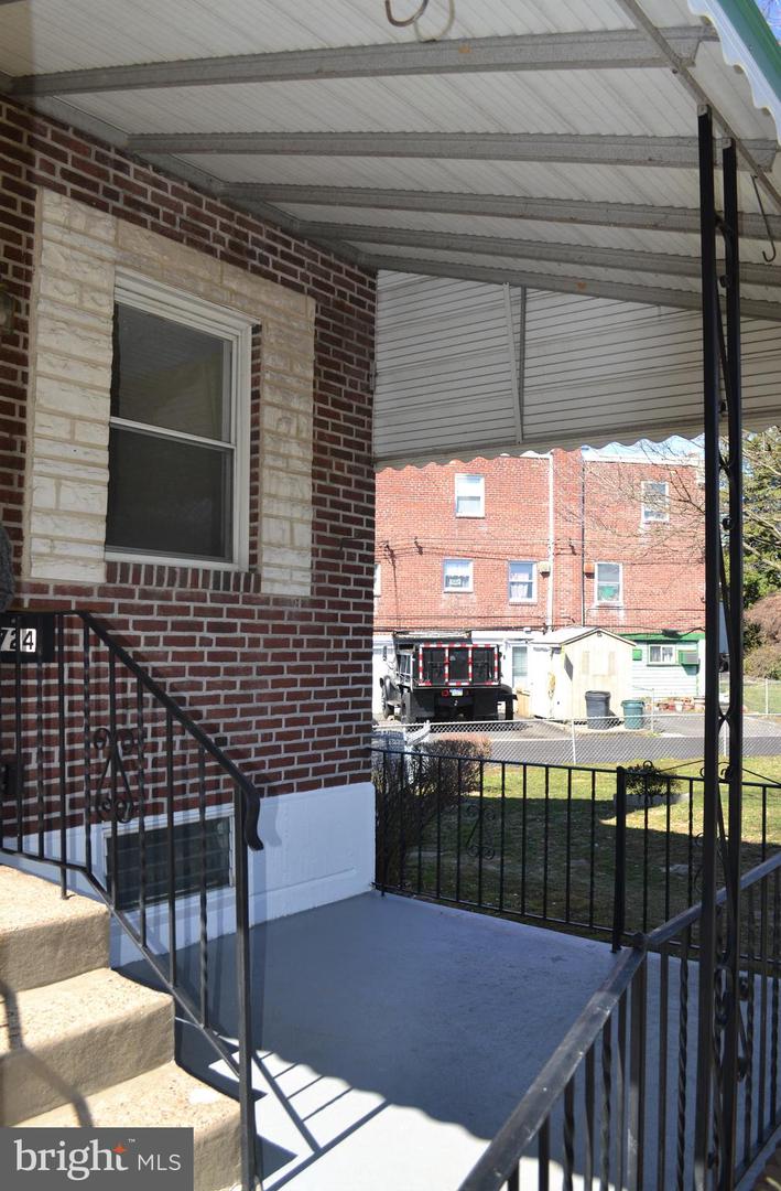 Covered front porch with concrete steps and black metal railings beside a brick exterior.