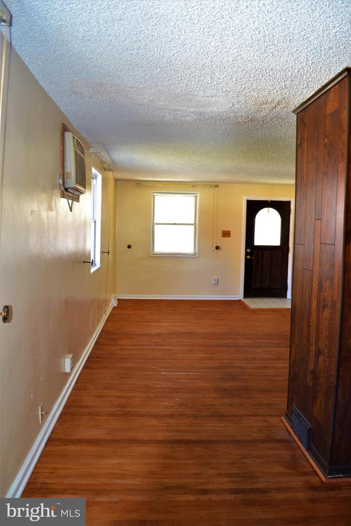 Empty room with reddish wood floors, a front door with arched glass, and a tall dark wood partition.