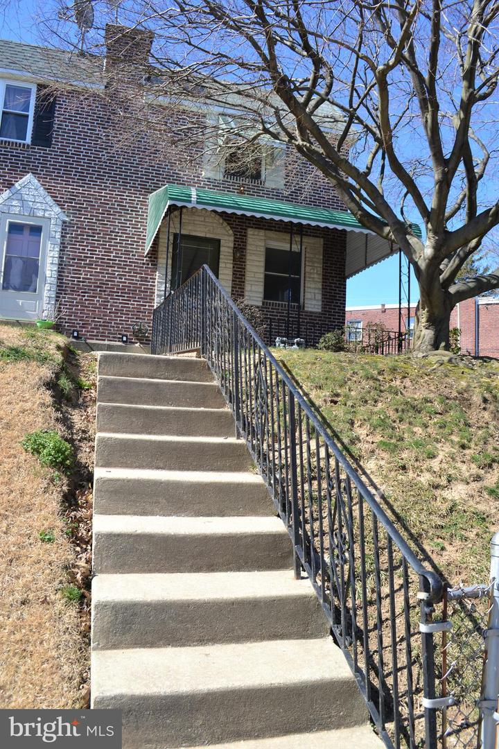 Brick home entrance above concrete steps, with a green awning and large leafless tree.