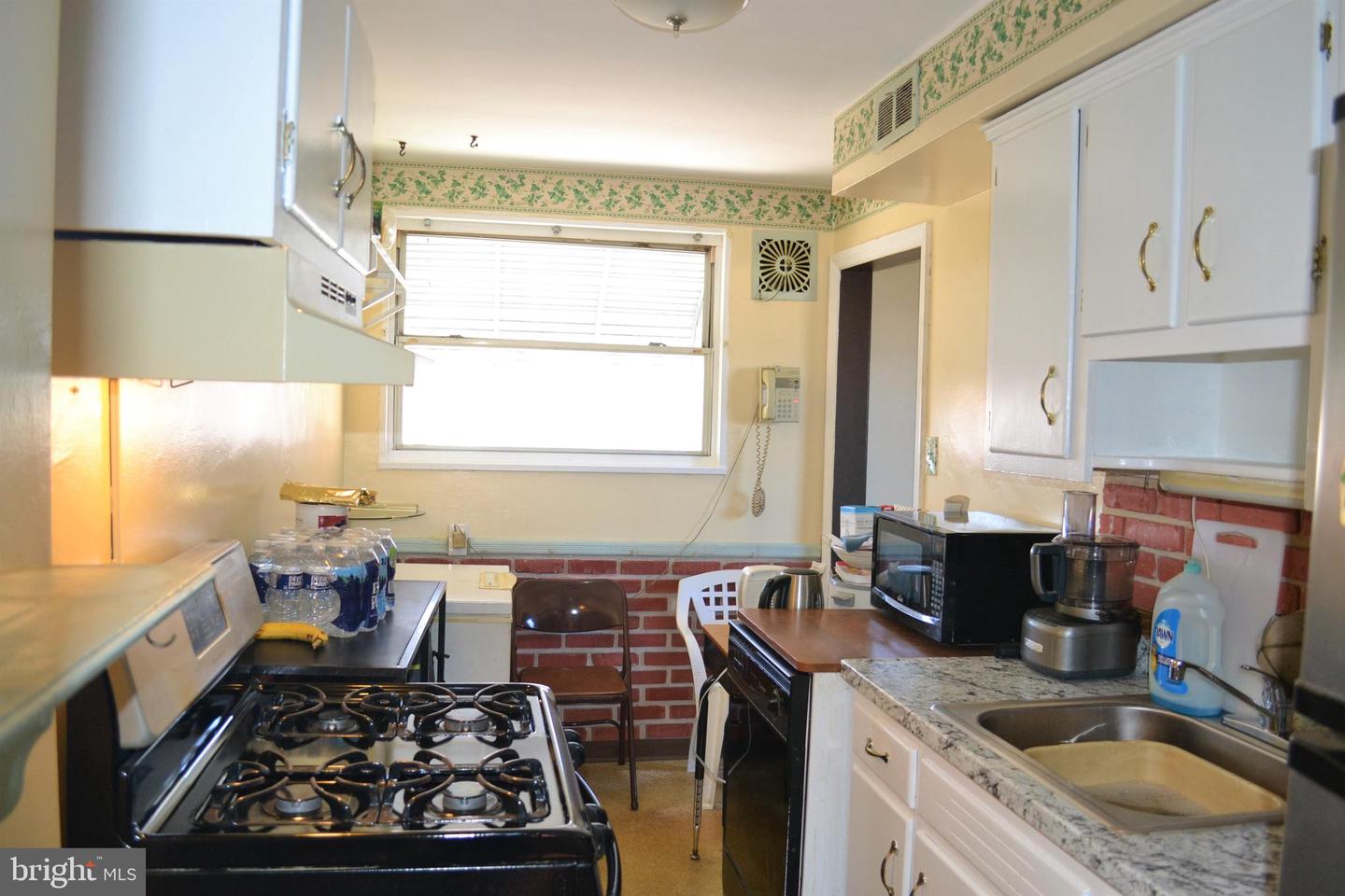 Narrow kitchen with white cabinets, a gas range, and a bright window above a brick-patterned backsplash.