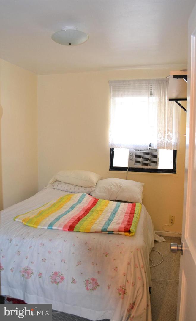 Bedroom with a floral bedspread, striped blanket, and window air conditioner.