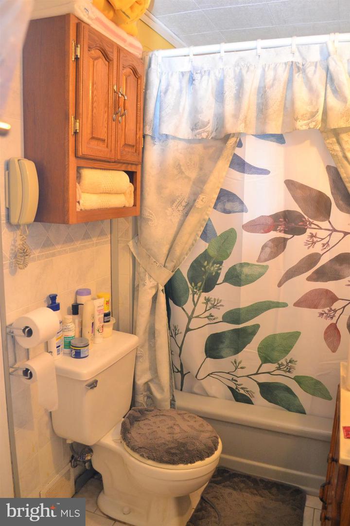 Bathroom with a leafy shower curtain, bathtub, toilet, and wooden wall cabinet.