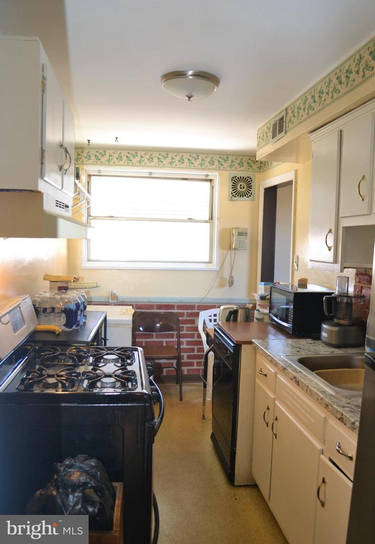 Narrow kitchen with black gas range, cream cabinets, granite counters, and brick backsplash.