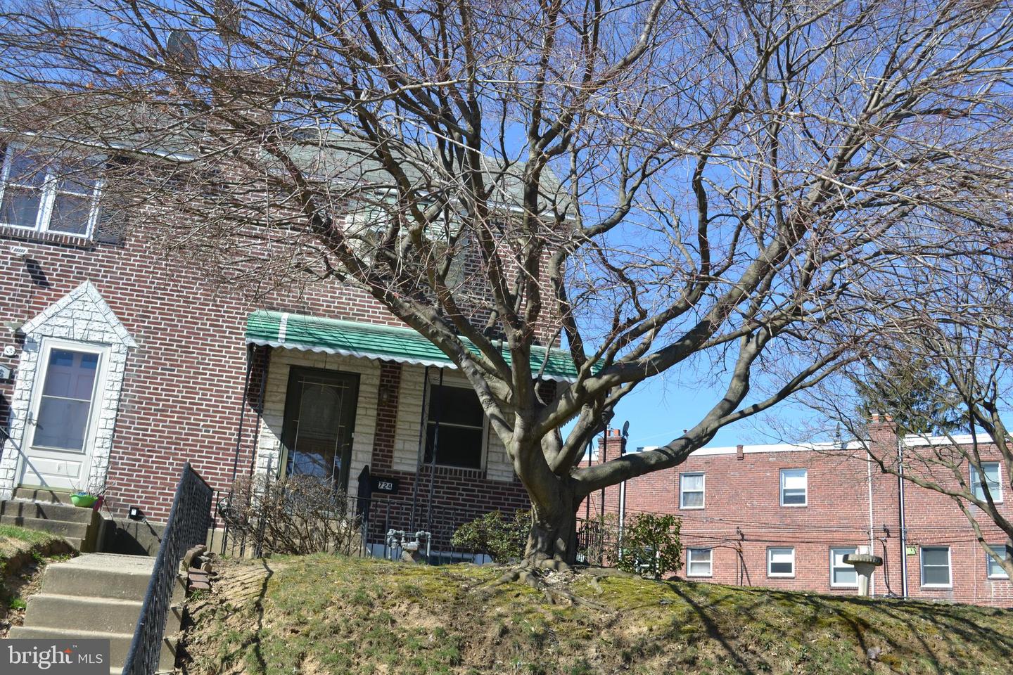 Red-brick home with a green entrance awning, front steps, and a large leafless tree.