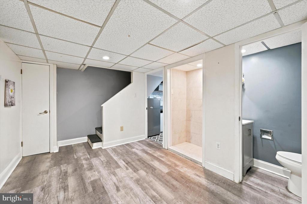 Finished basement with wood-look floors, stairs, a tiled shower, and a separate toilet room.
