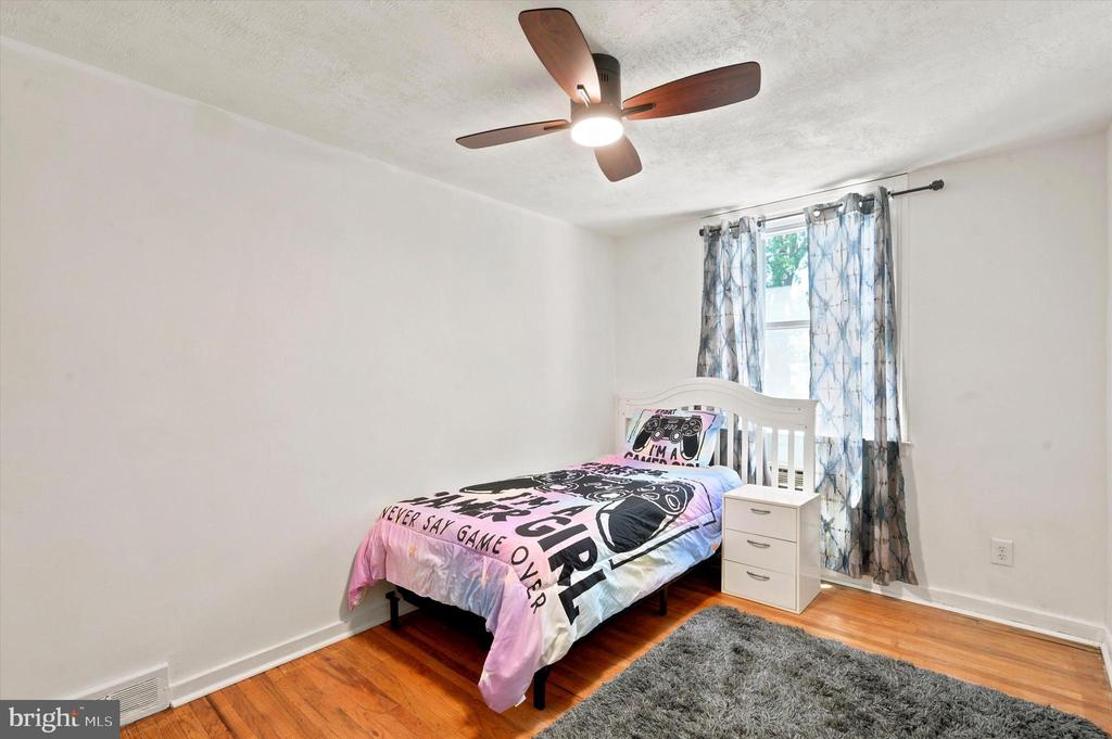Bedroom with gaming-themed bedding, blue curtains, hardwood floors, and a gray rug.