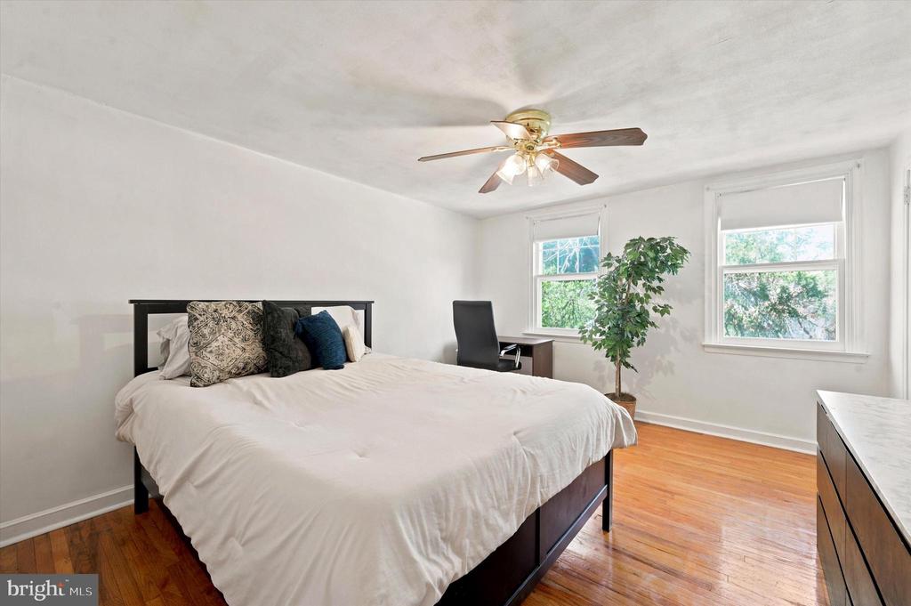 Bedroom with a large bed, polished hardwood floors, and two bright windows.