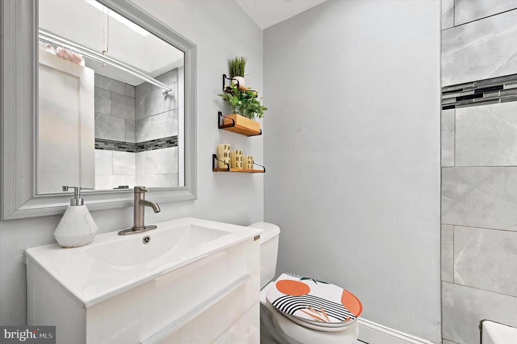 Bathroom with a white vanity, framed mirror, gray tiled shower, and colorful toilet lid.