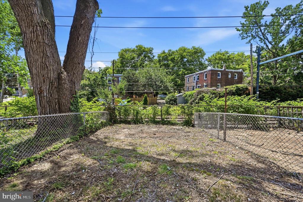 Fenced backyard with a large tree and neighboring homes beyond the fence.