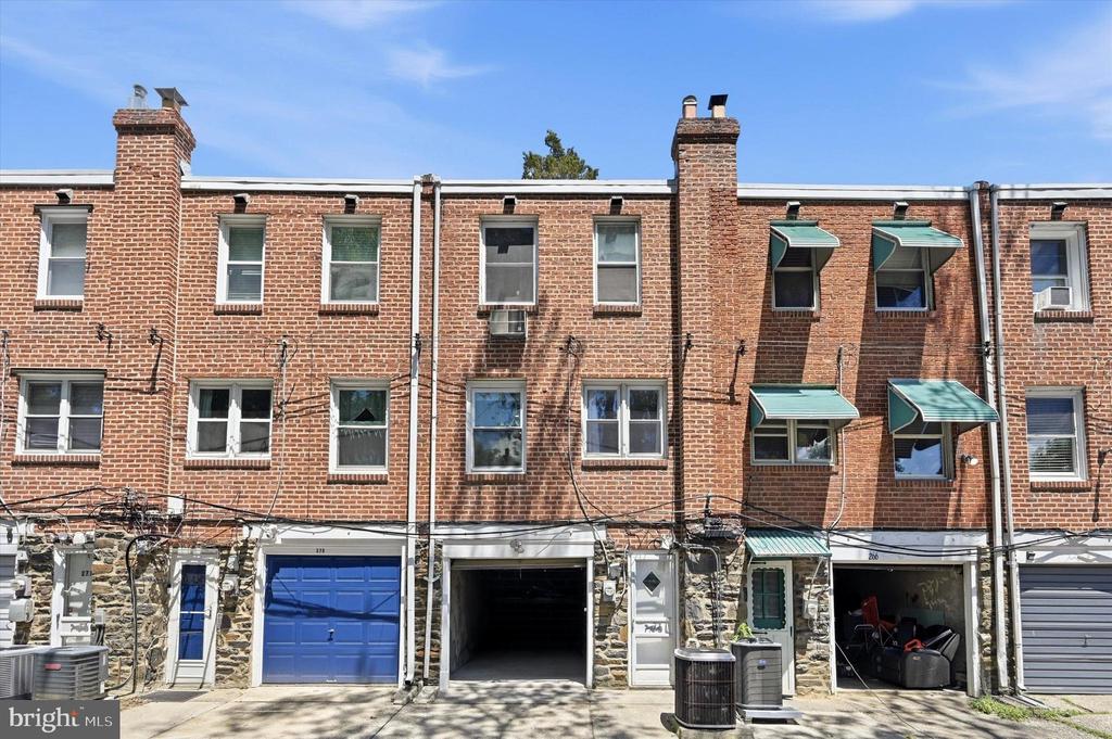 Brick rowhouse facade with ground-level garages and green window awnings.