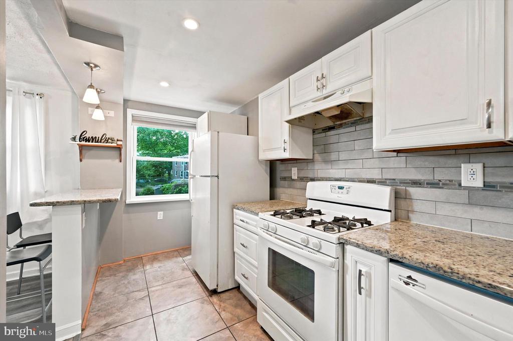Kitchen with white cabinets, granite counters, a gas range, and gray subway-tile backsplash.