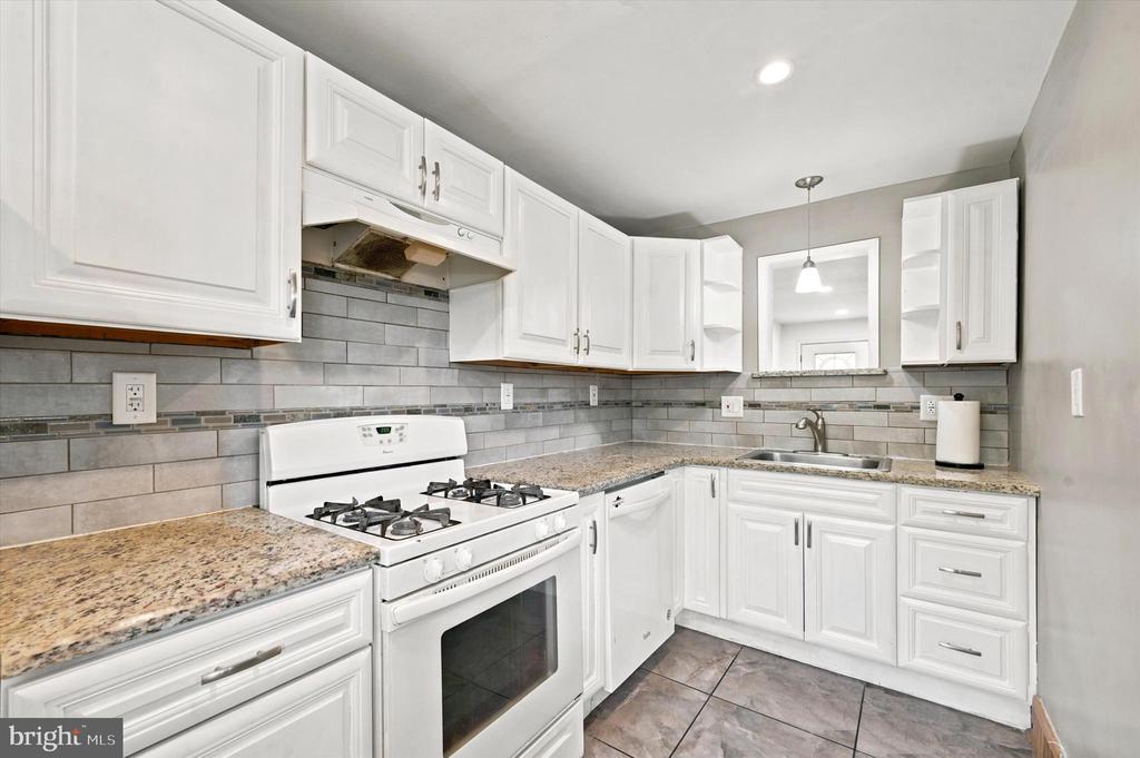 Kitchen with white cabinets, gray tile backsplash, granite counters, and a white gas range.