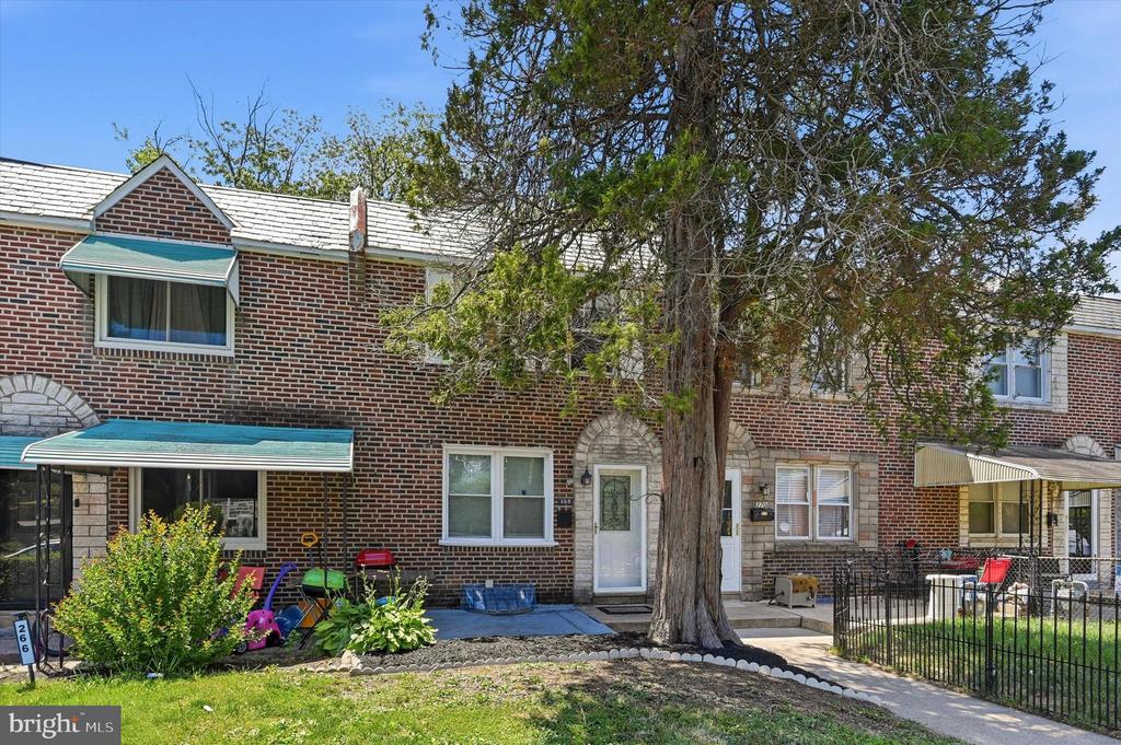 Brick rowhouse with green awnings, partly shaded by a large tree beside the front walkway.