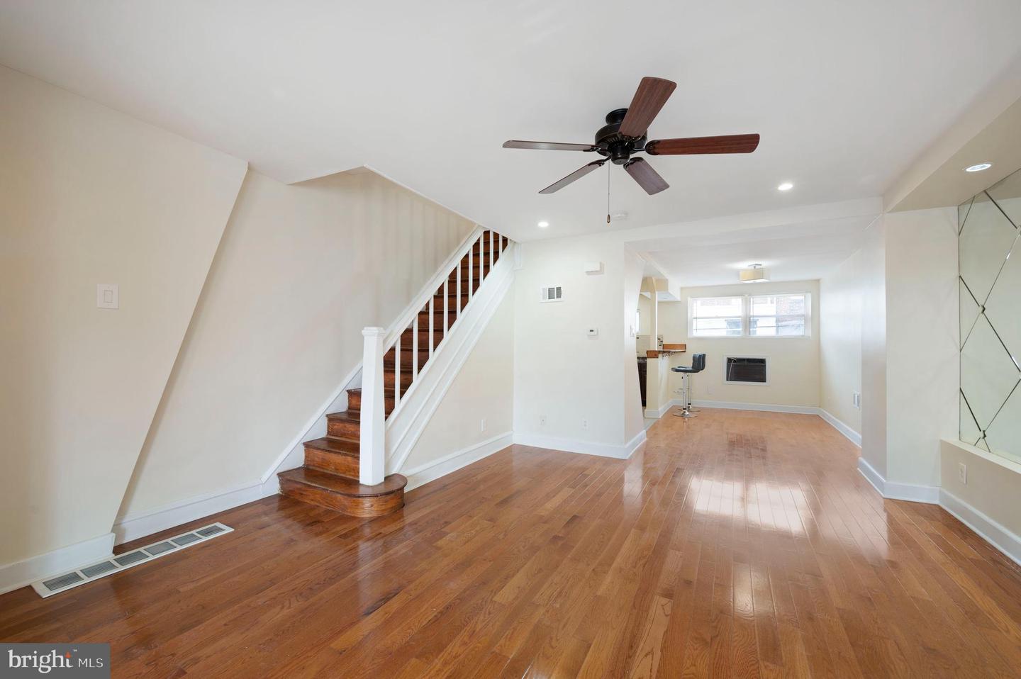 Empty living area with hardwood floors, a wood-tread staircase, and a ceiling fan.