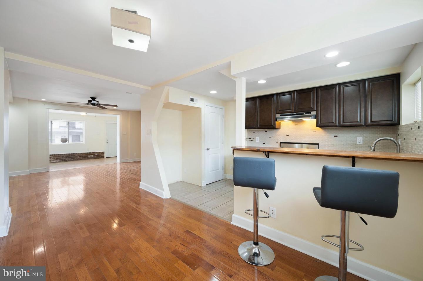 Open-plan kitchen with dark wood cabinets and breakfast bar beside a hardwood-floored living area.